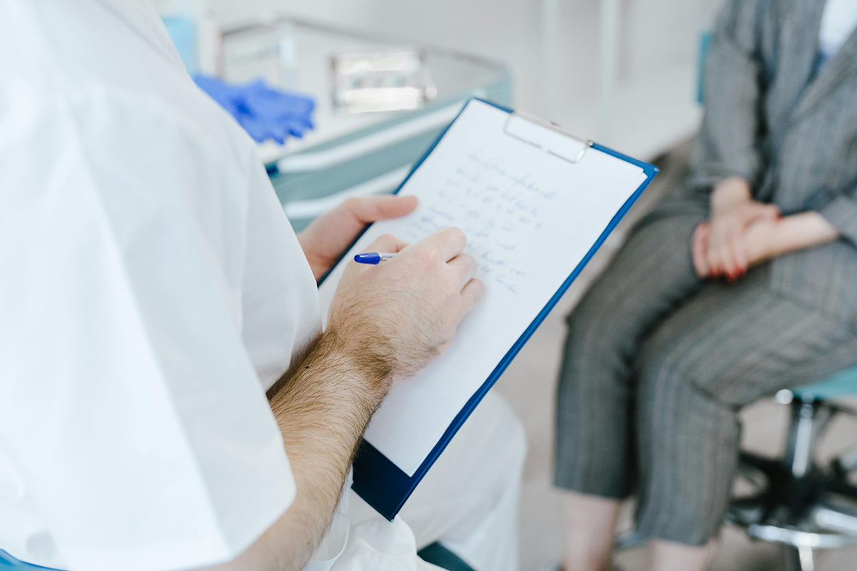 A person with a clipboard writes on a piece of paper with another person in the background